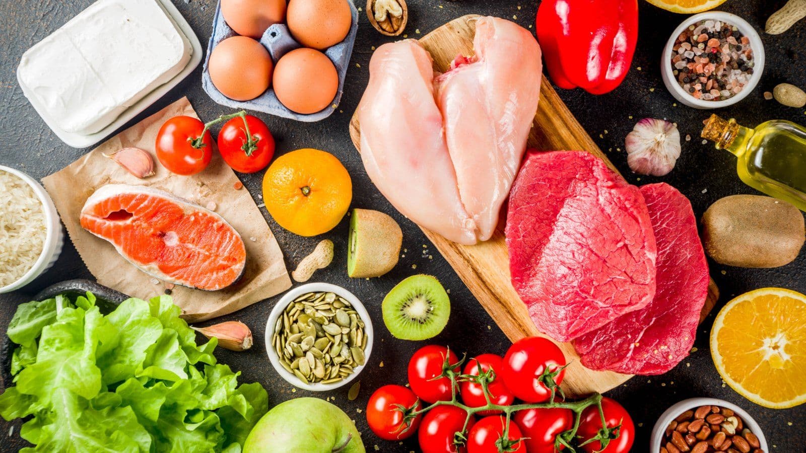 Poisson, viande, oeufs, laitages et legumes frais disposes sur un plan sombre