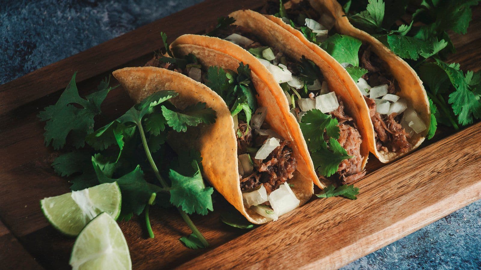 Trois tacos garnis de viande et coriandre sur une planche en bois