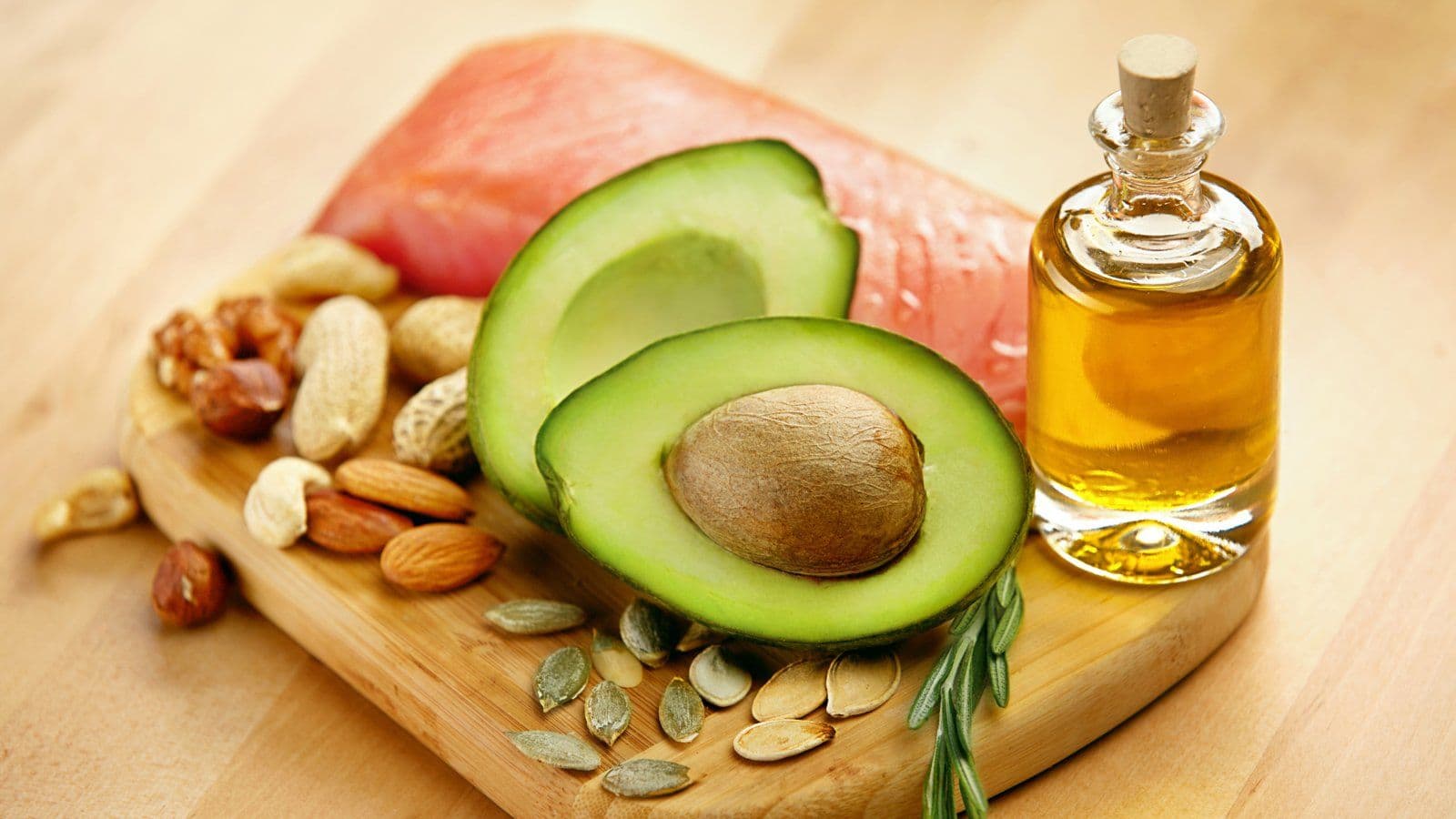 Avocat coupe en deux, saumon, oleagineux et flacon d huile sur planche