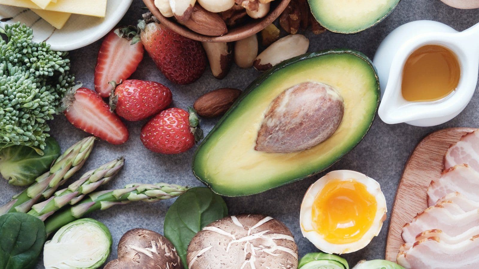 Avocat, oeuf, asperges, fraises et poisson disposes sur fond sombre