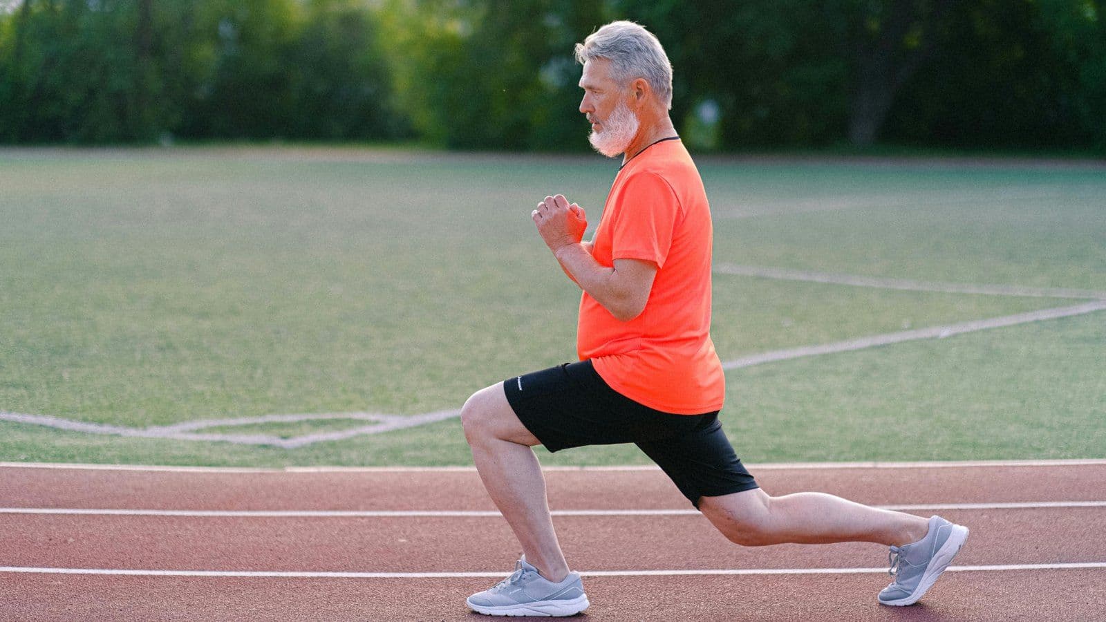 Homme senior en tenue de sport realisant une fente sur une piste