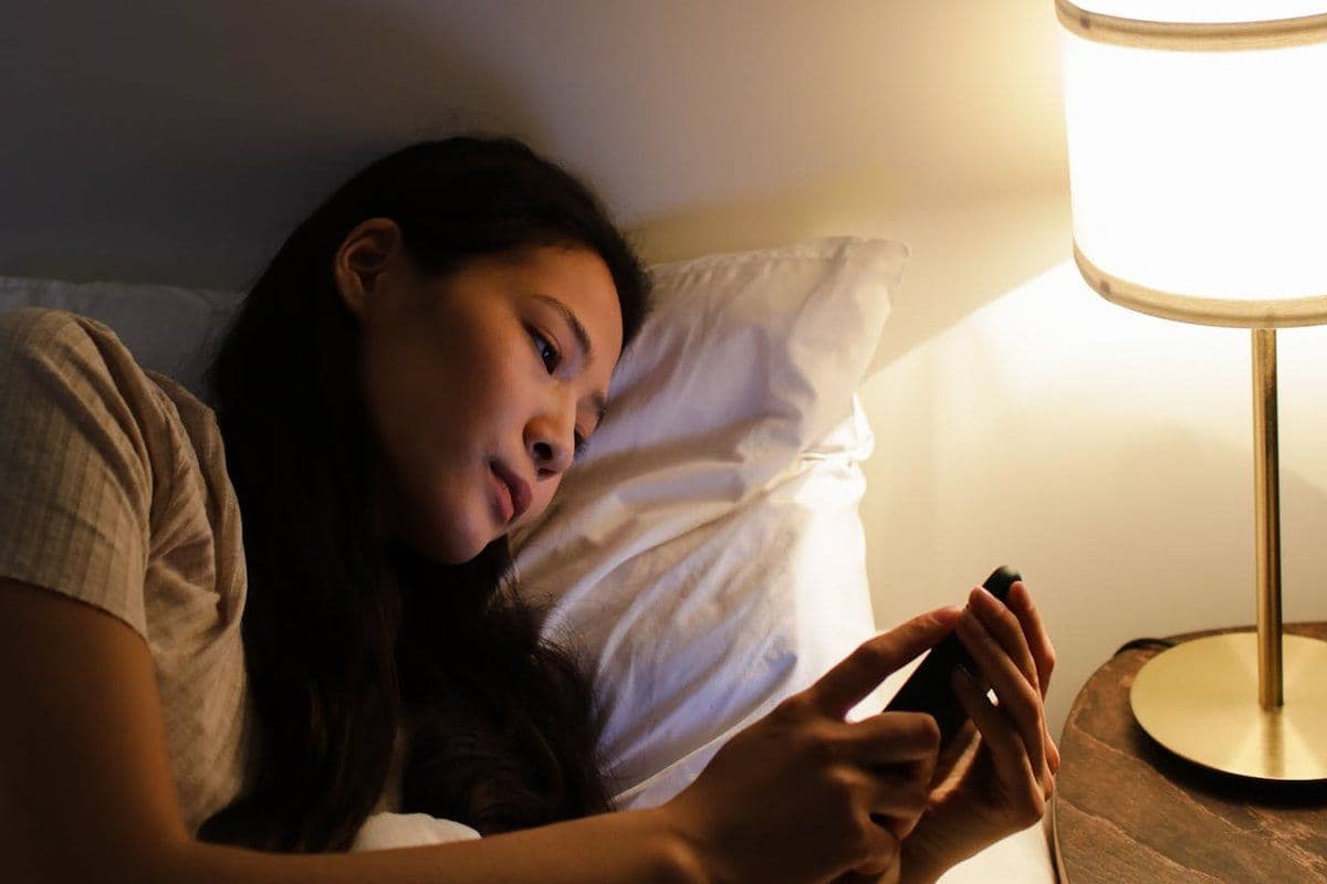 Personne consultant son téléphone le soir au lit, lumière de chevet