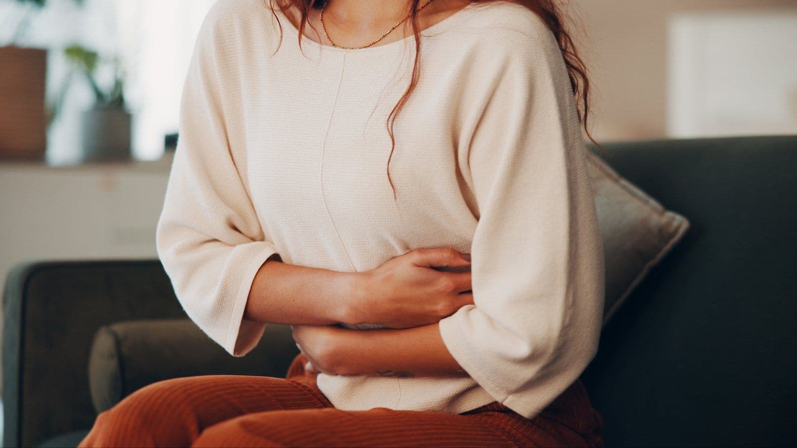 Femme assise sur un canape, les bras replies sur le ventre douloureux