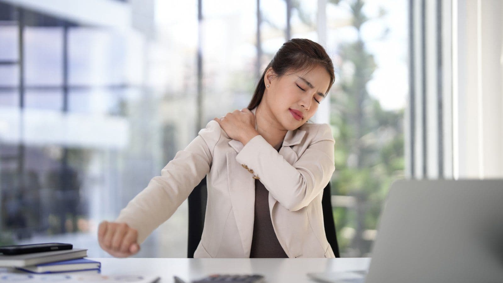 Femme au bureau se tenant l epaule avec une grimace de douleur