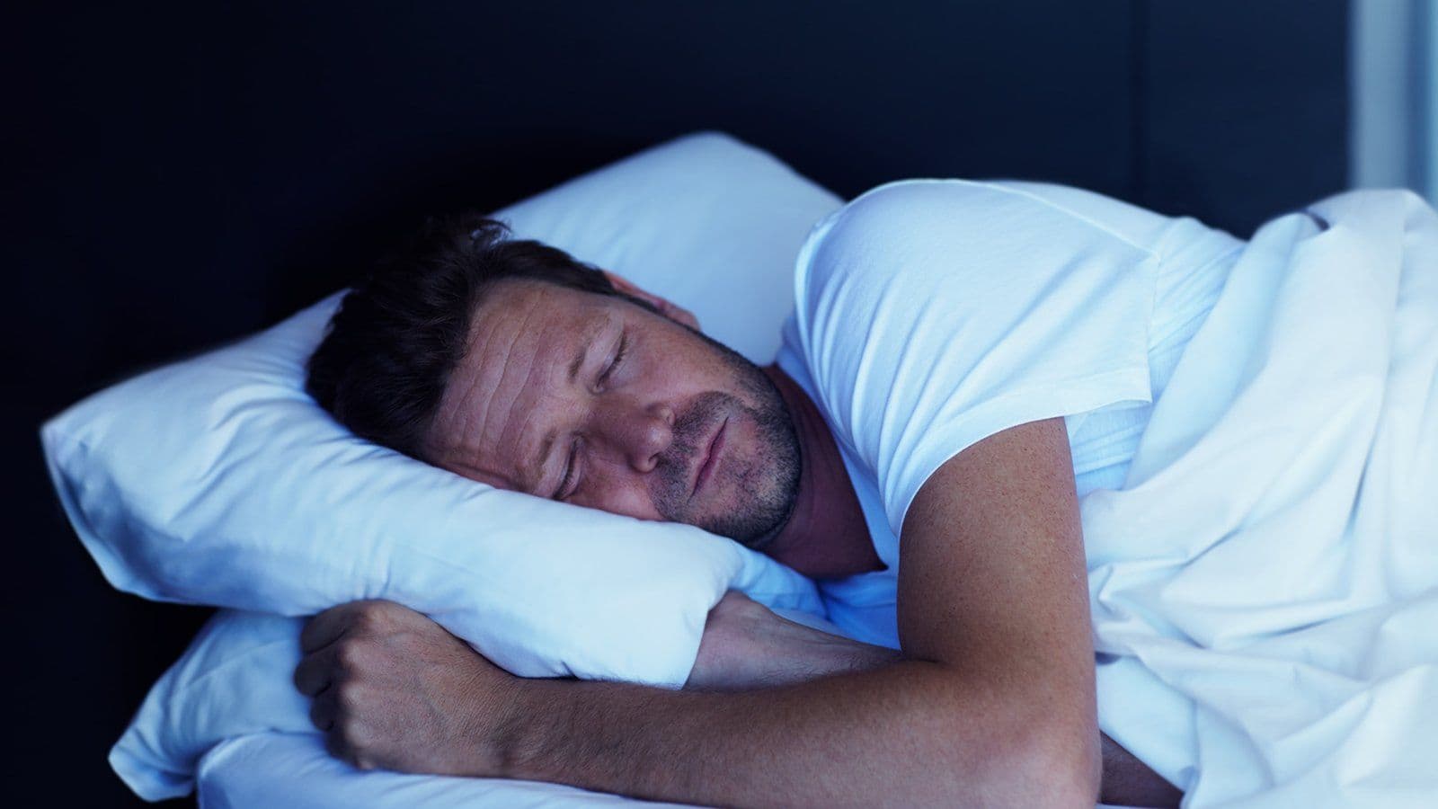 Homme endormi paisiblement dans un lit aux draps clairs