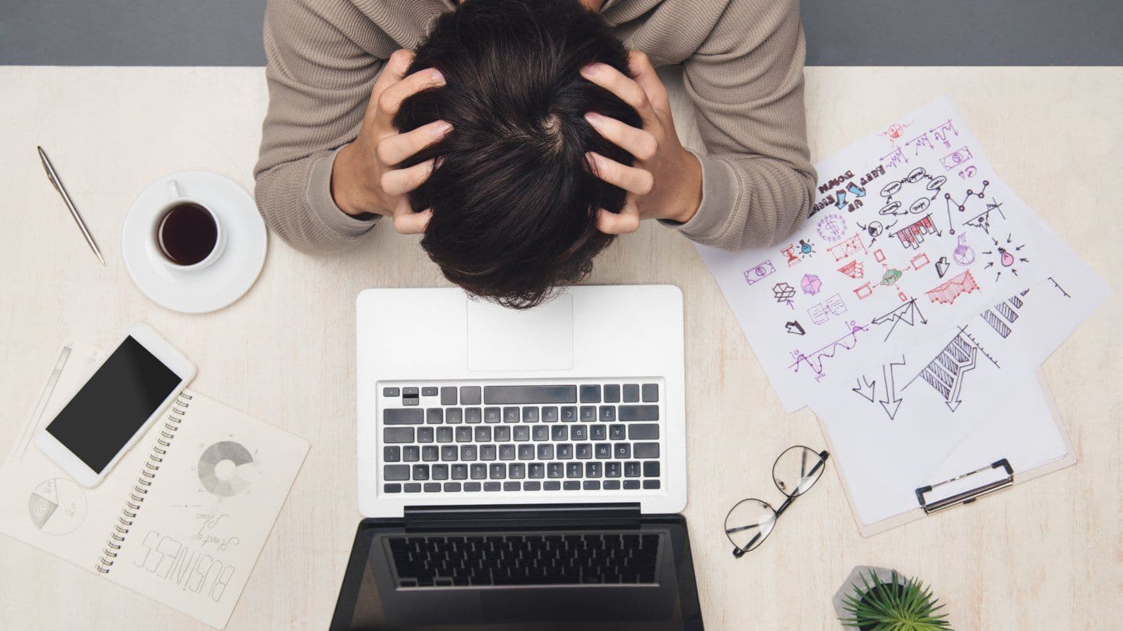 Personne effondree sur son bureau, les mains dans les cheveux, vue de dessus