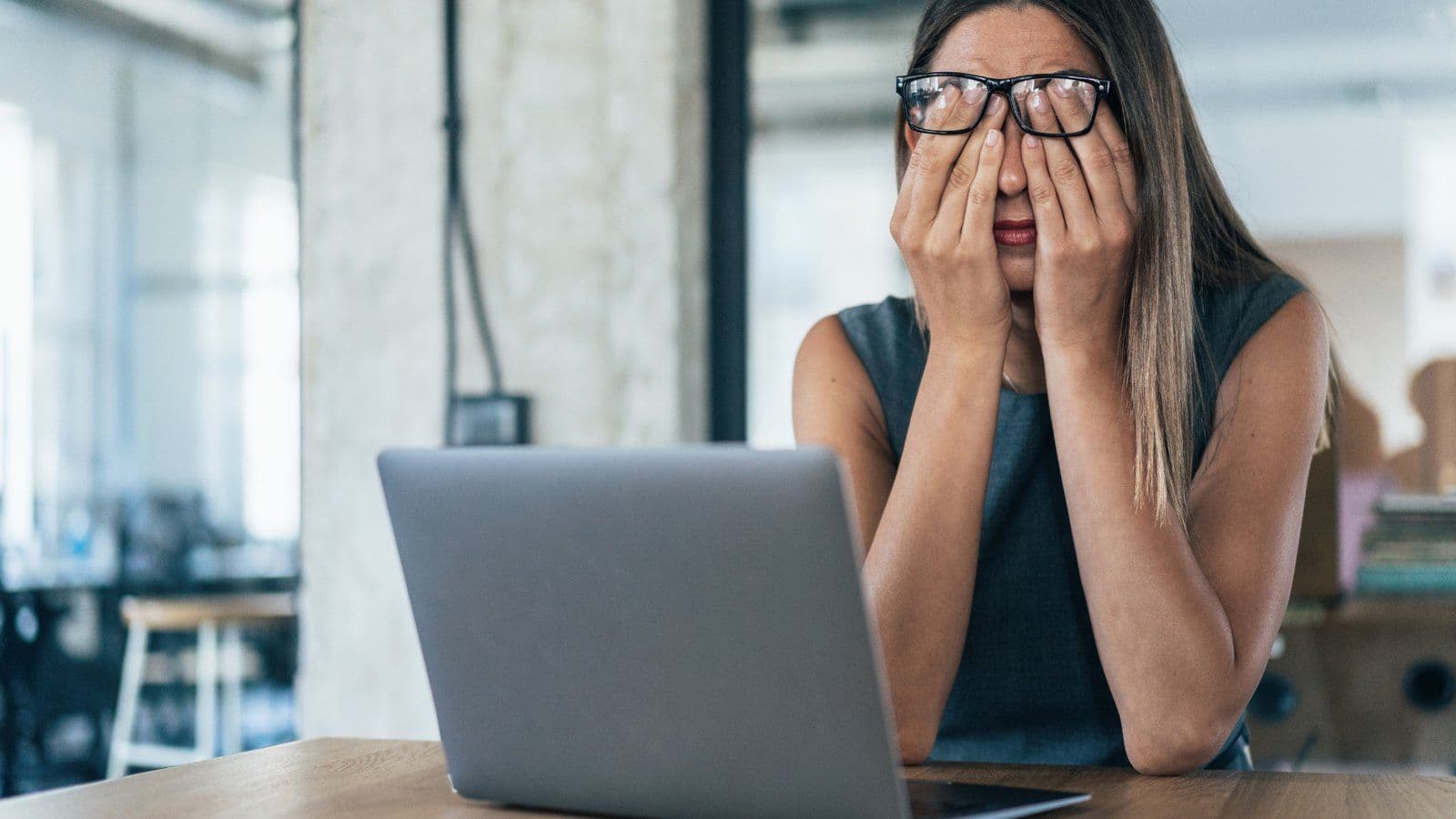 Femme se couvrant le visage des deux mains devant son ordinateur portable
