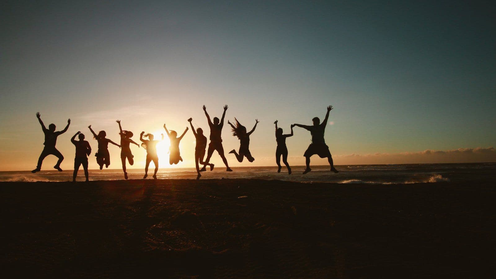 Groupe de personnes sautant les bras leves au coucher du soleil