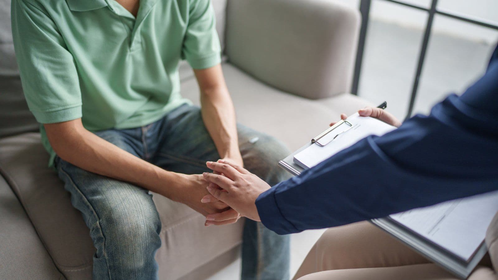 Mains d une personne serrees, face a un professionnel prenant des notes