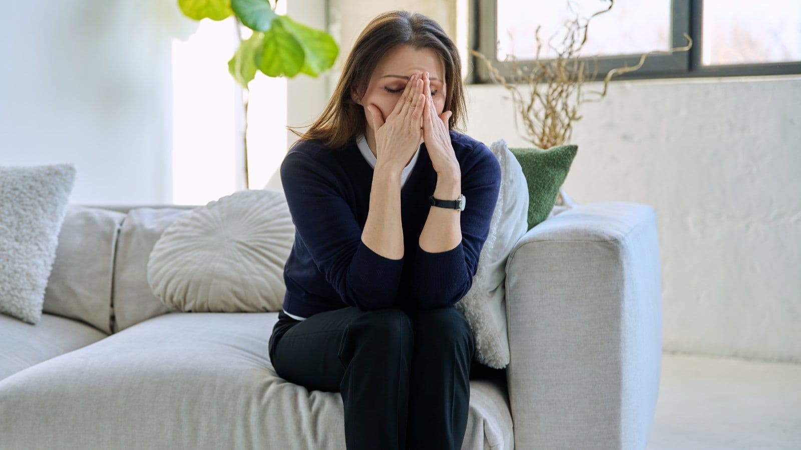 Femme assise sur un canape, le visage cache dans ses mains