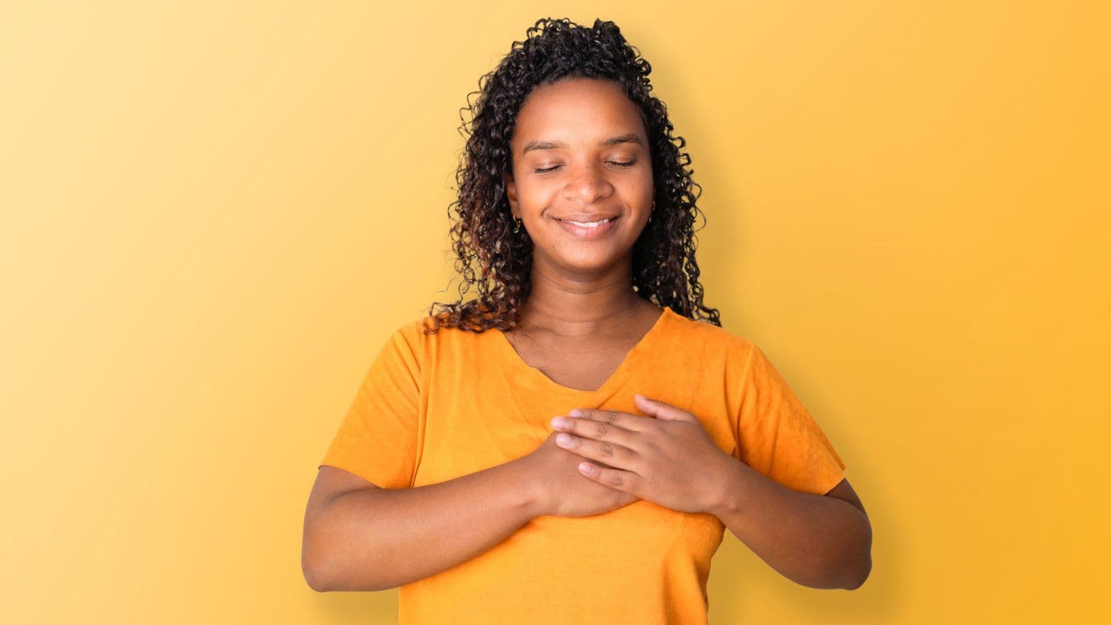 Femme souriante les mains posees sur le coeur, sur fond jaune