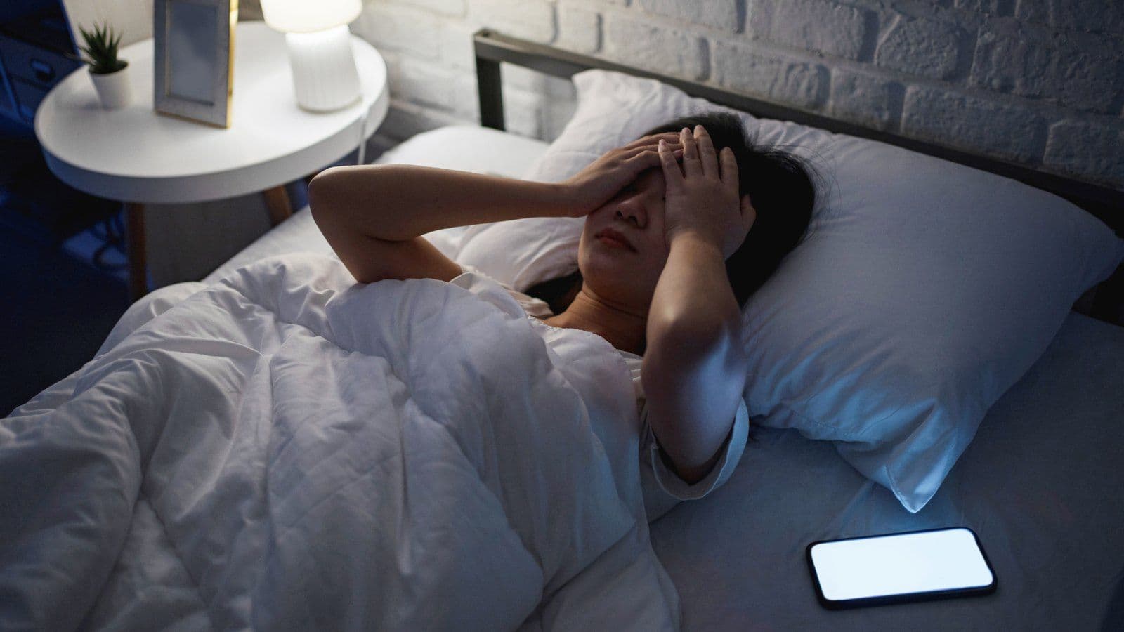 Femme eveillee au lit, la main sur le front, smartphone allume a cote d'elle