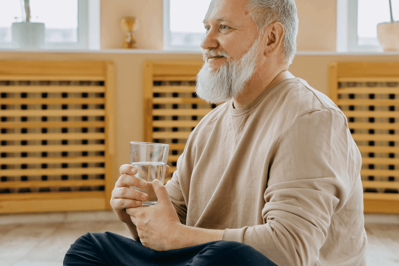 Homme senior souriant tenant un verre d eau, assis pres d un radiateur