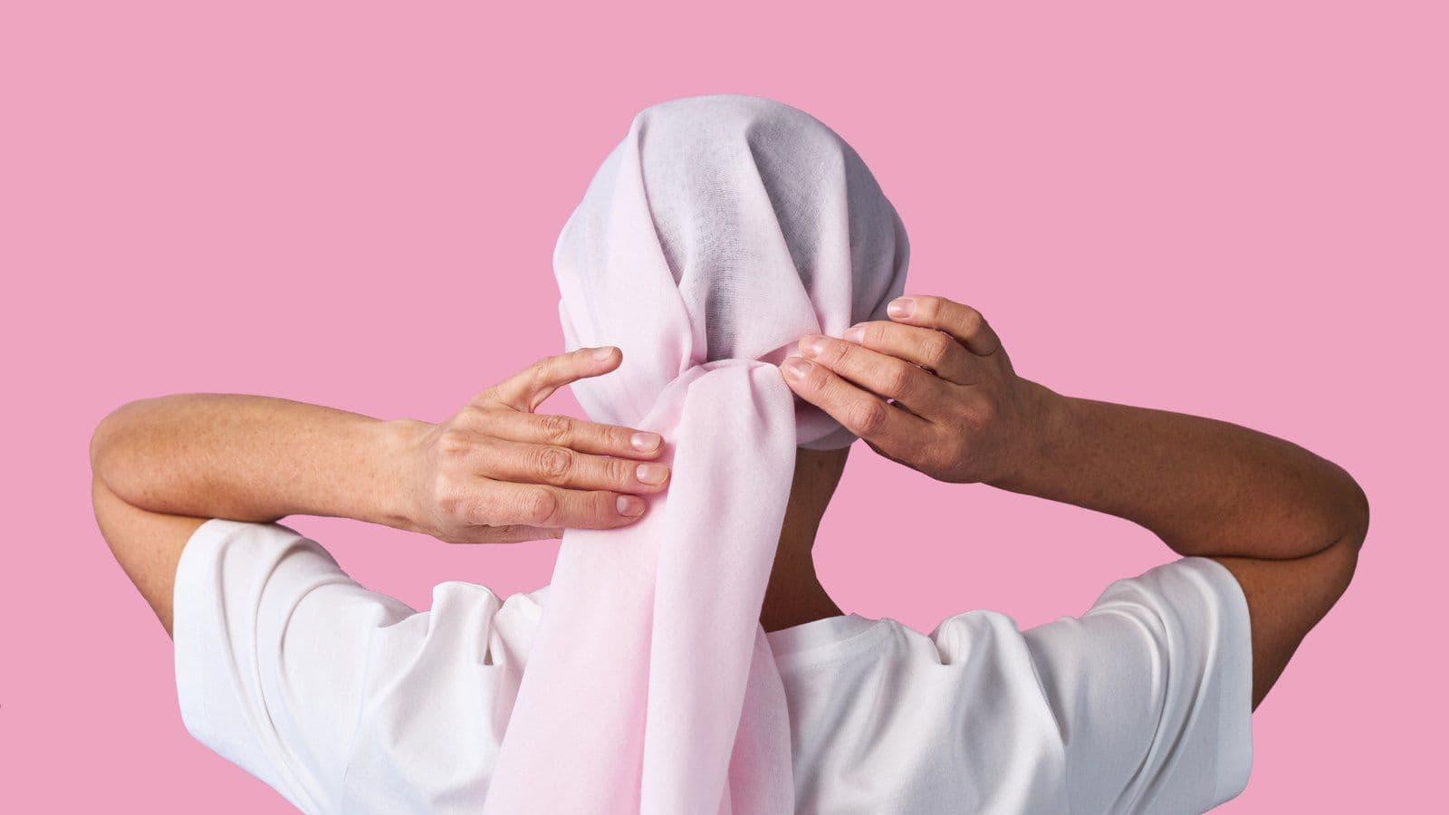 Personne ajustant un foulard rose sur sa tete, vue de dos