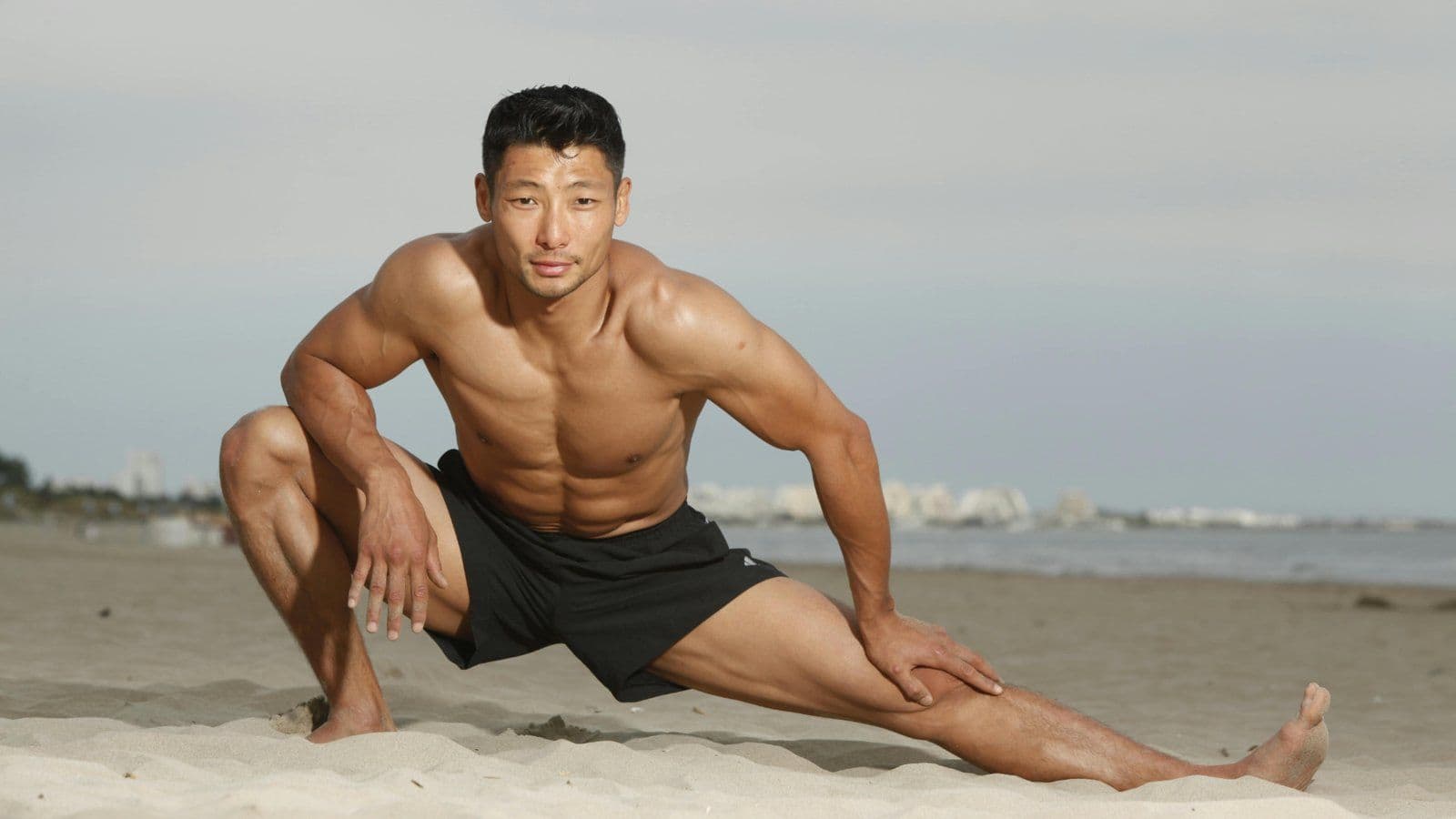 Homme torse nu realisant un etirement assis sur le sable
