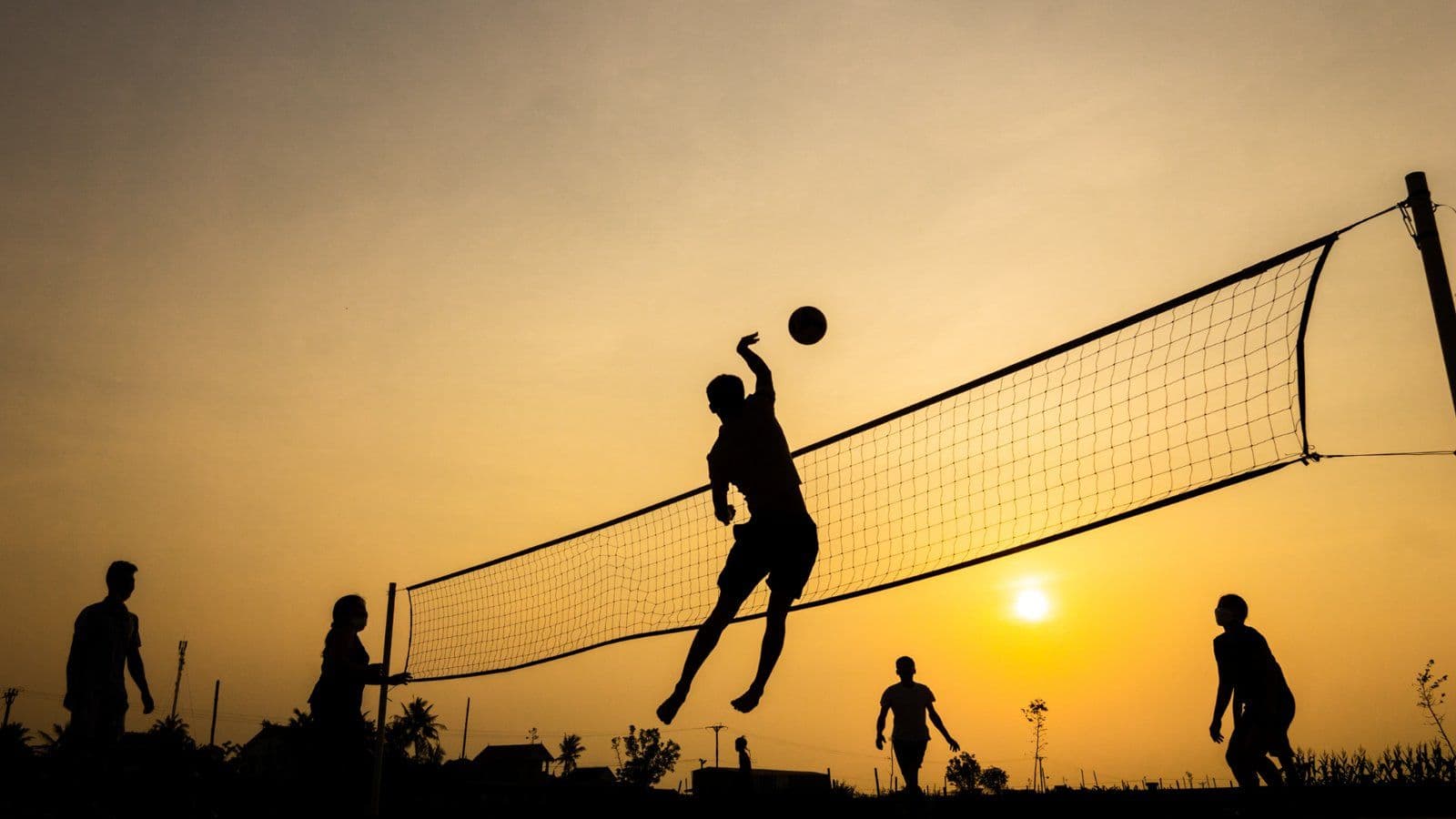 Silhouettes de joueurs de volley-ball au filet au coucher du soleil