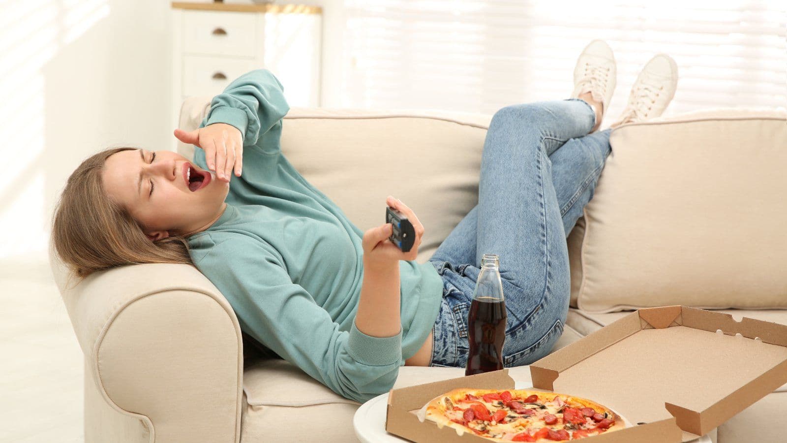 Femme allongee sur un canape grignotant devant une boite de pizza