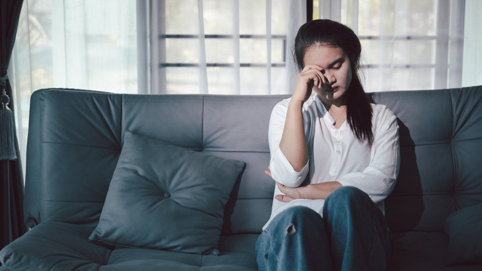 Femme assise seule sur un canape, la main contre la tempe