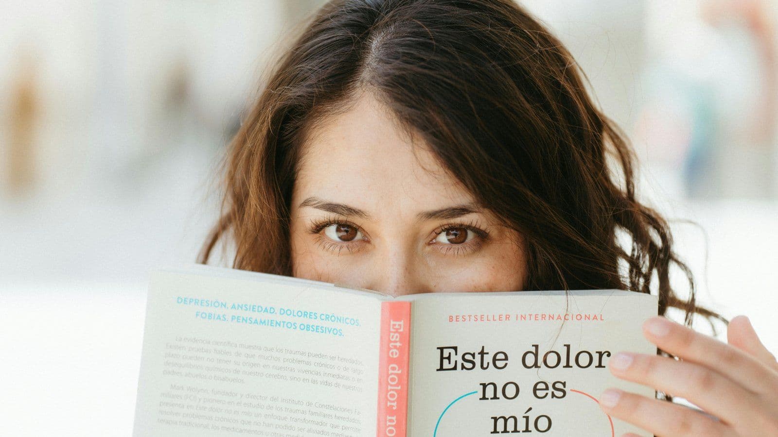 Femme tenant un livre devant son visage, regard vers l objectif