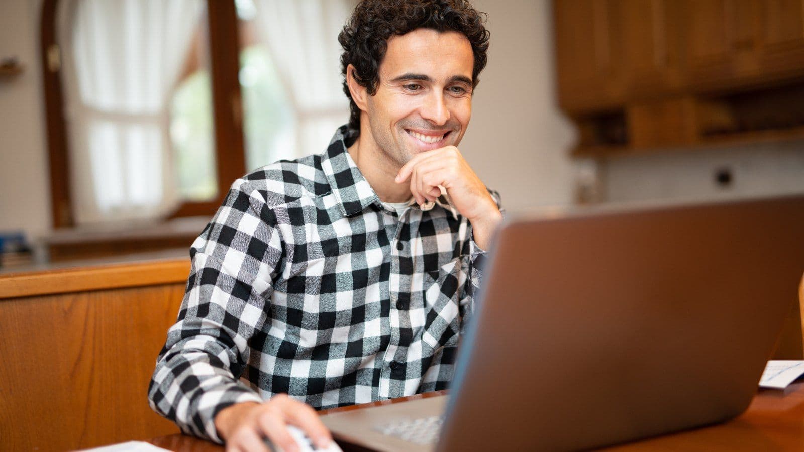 Homme souriant travaillant sur son ordinateur portable depuis sa cuisine