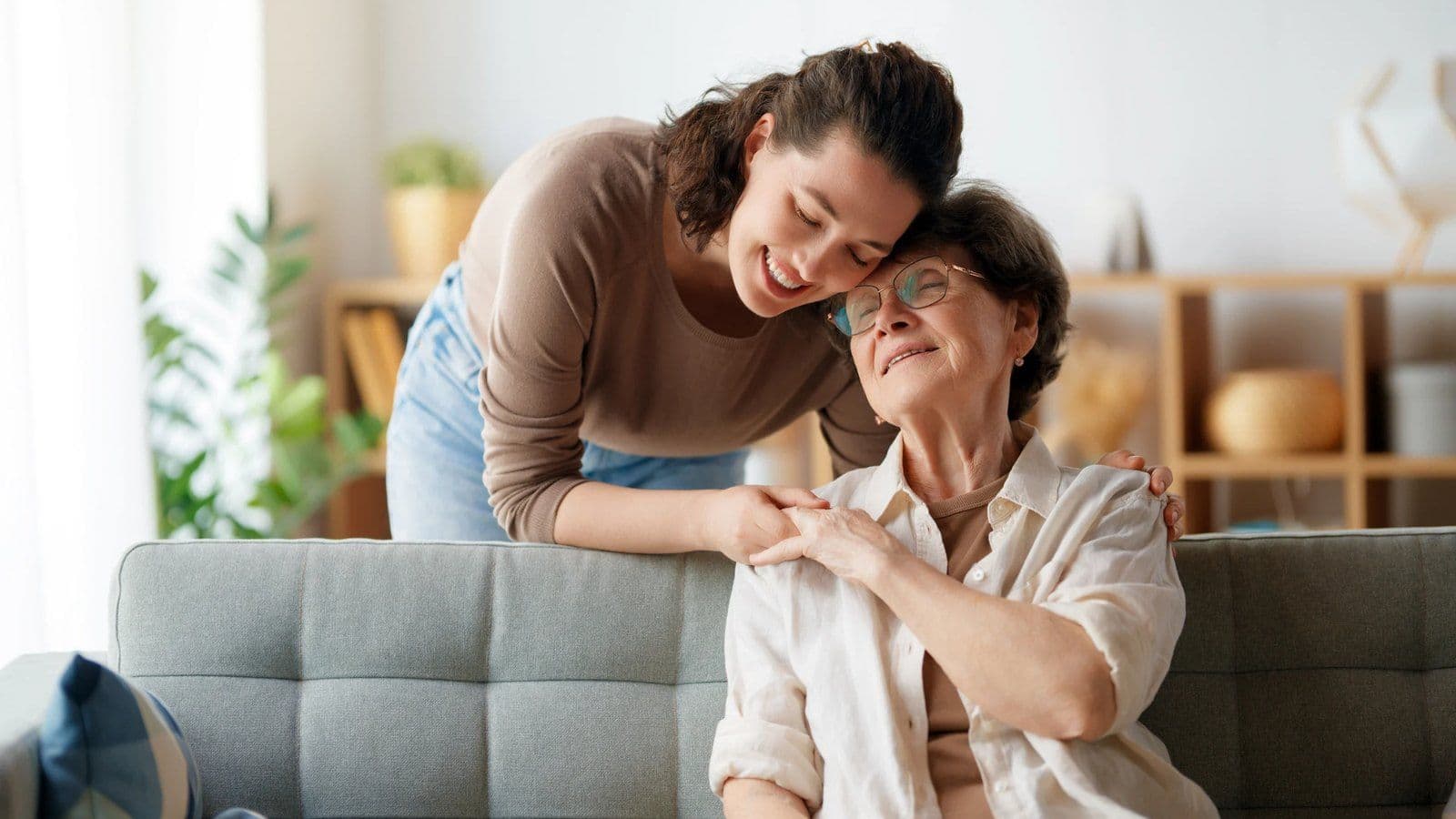 Jeune femme entourant affectueusement sa mere agee assise sur un canape