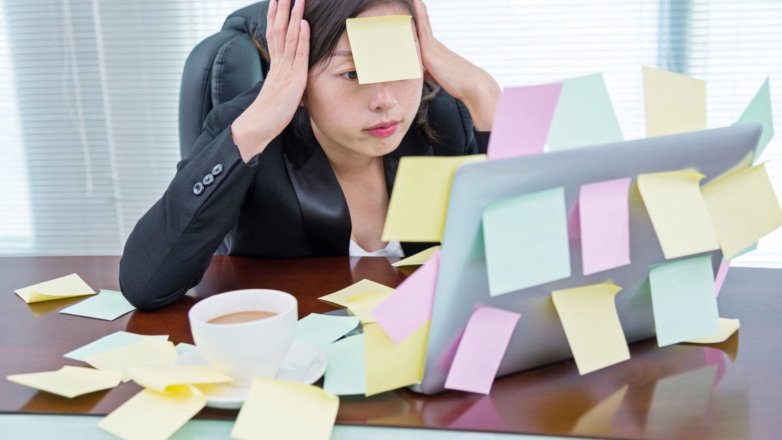 Femme debordee a son bureau, entouree de pense-betes colles partout