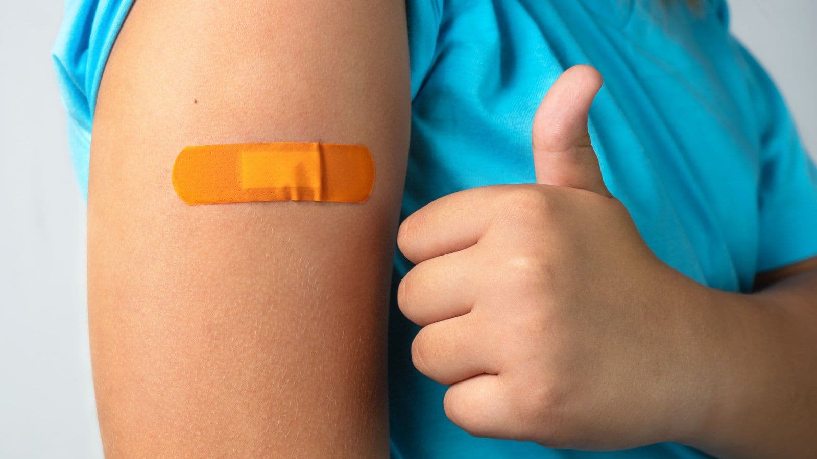 Bras portant un pansement orange apres une vaccination, pouce leve